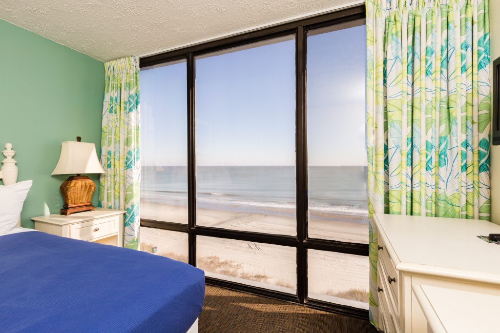 A beach view room with a blue bedspread and white furniture.