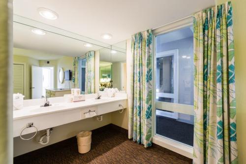 A wide bathroom with a double vanity, large mirror, and window with curtains.
