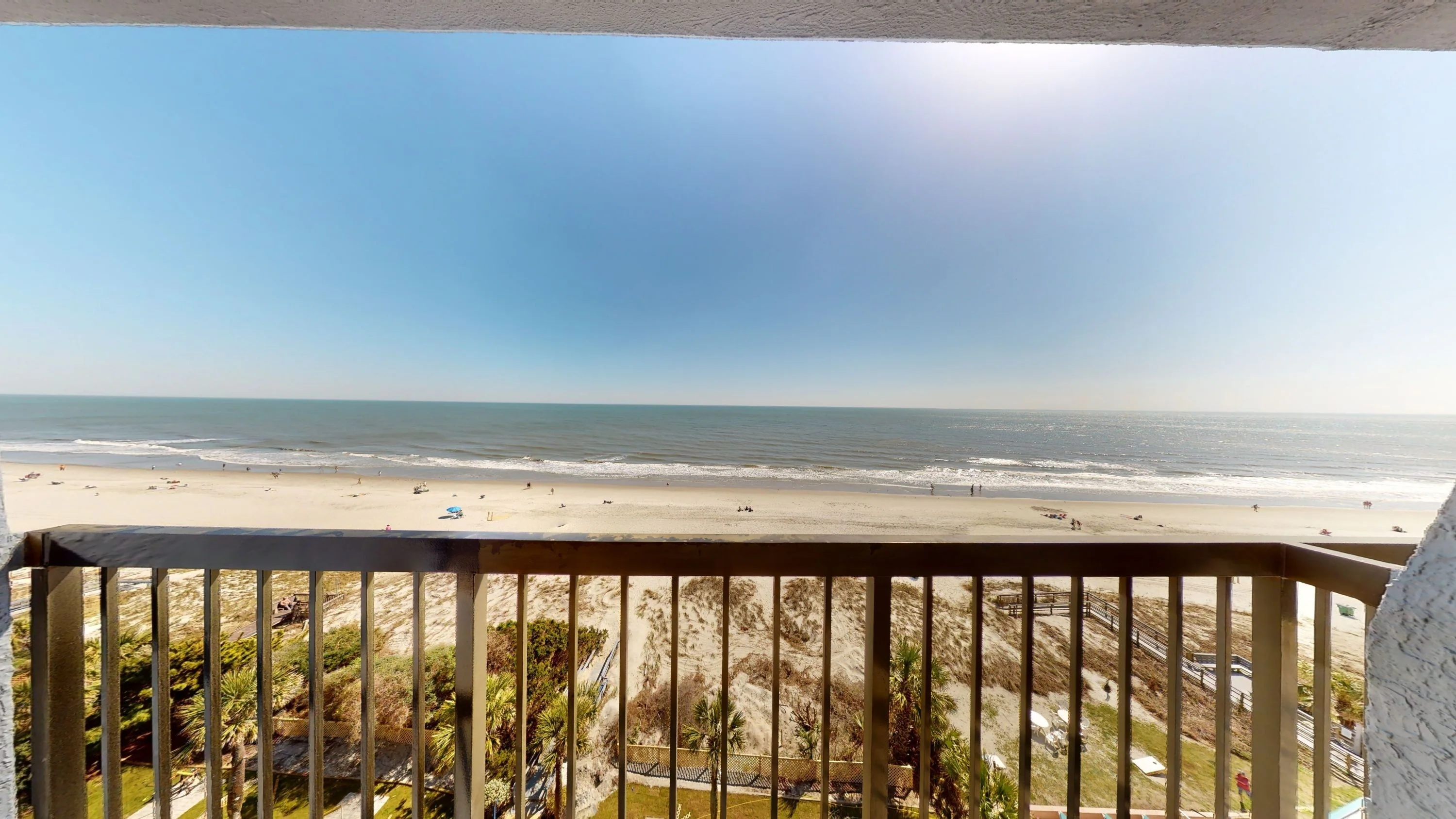 A balcony with a railing overlooking a beach and the ocean.