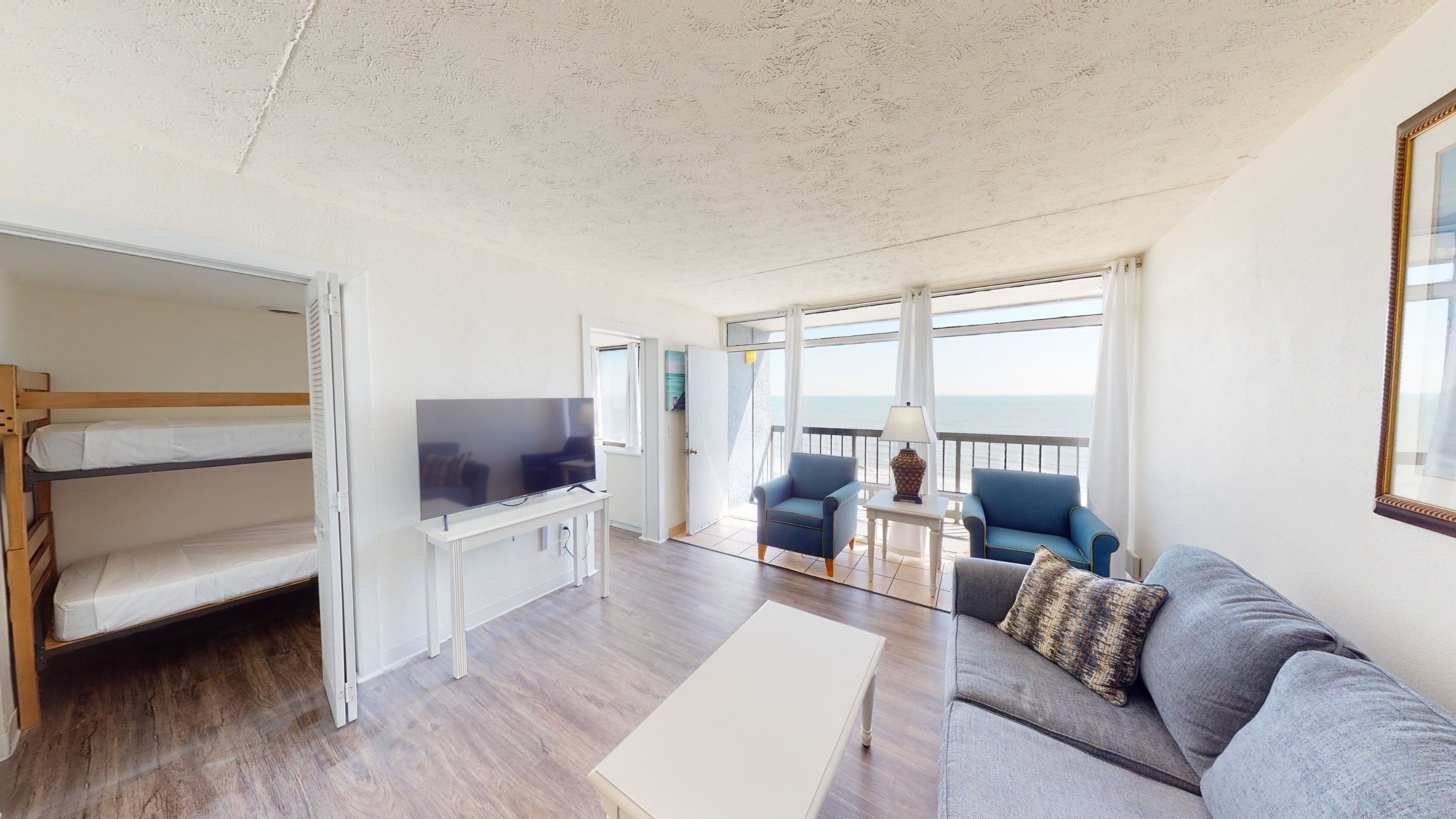 A wide view of a suite with bunk beds, a sofa, TV, and balcony with ocean view.