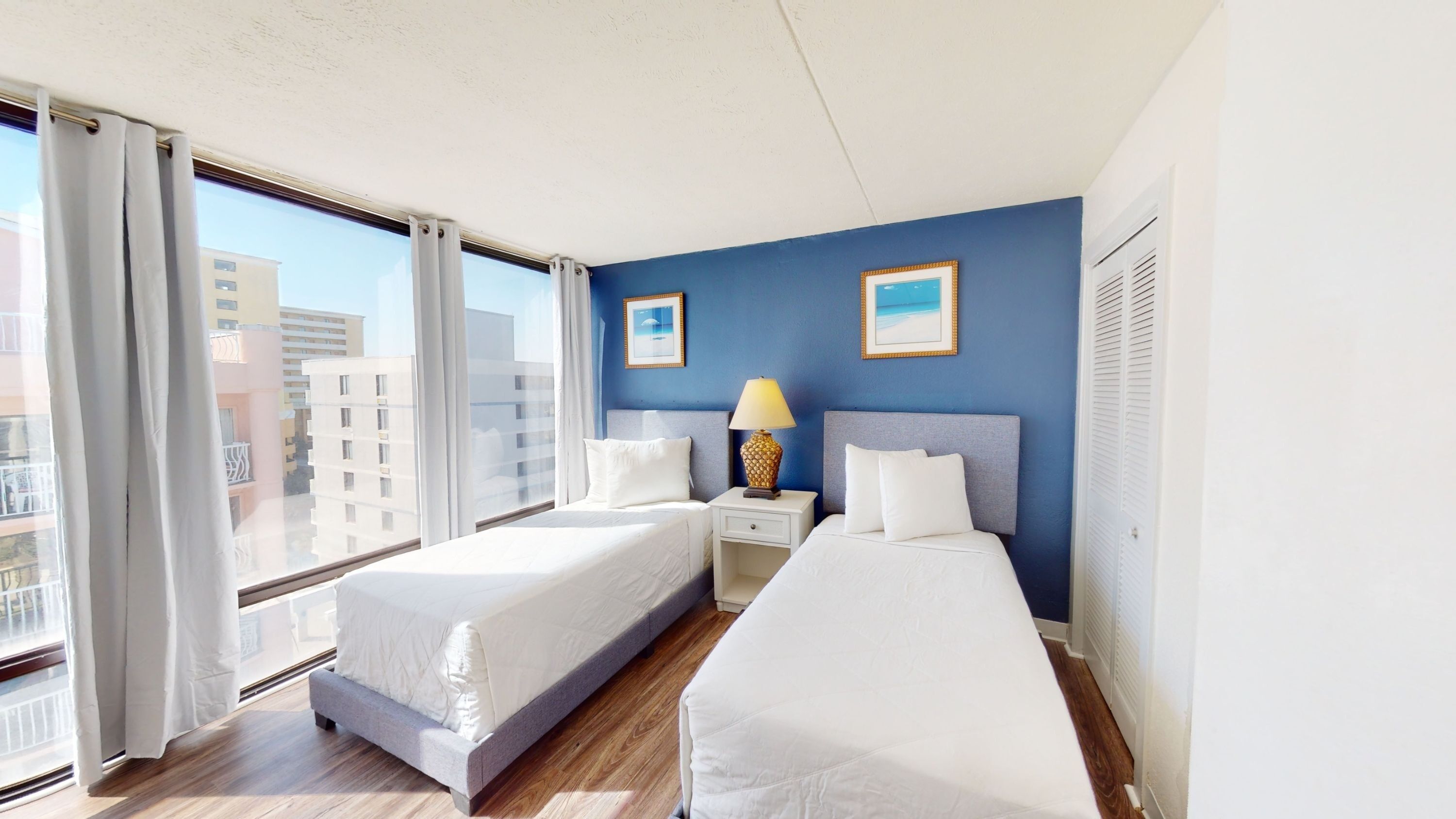 A hotel room with two twin beds, a blue accent wall, and a large window overlooking the city.