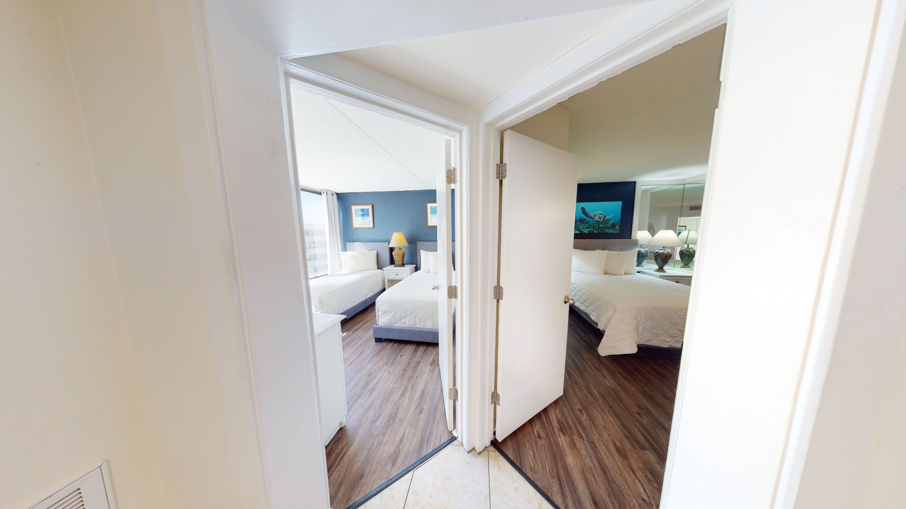 A wide view of a hotel room with two beds, a TV, and a doorway.