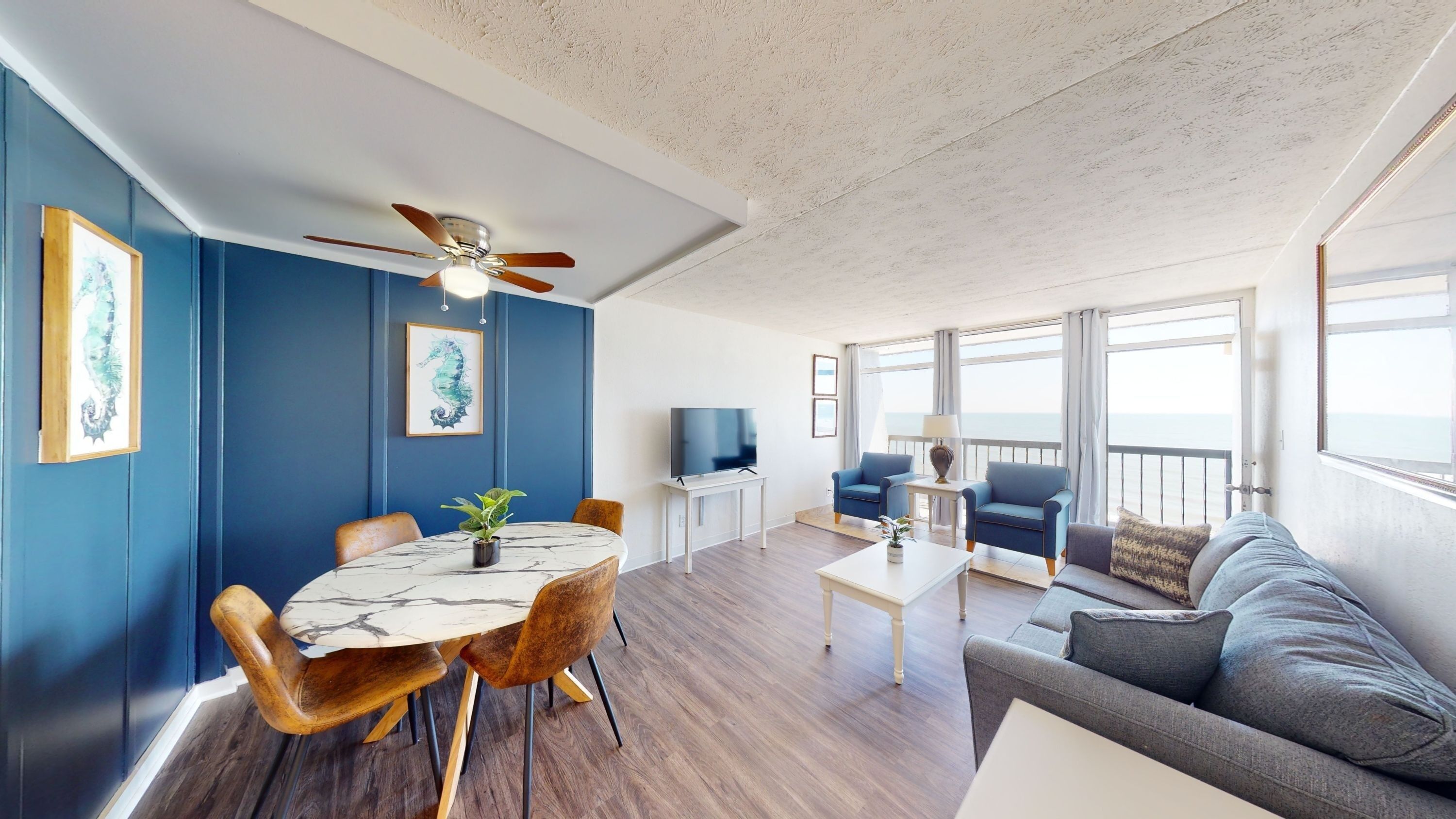 A wide view of a living room and dining area with a balcony and ocean view.