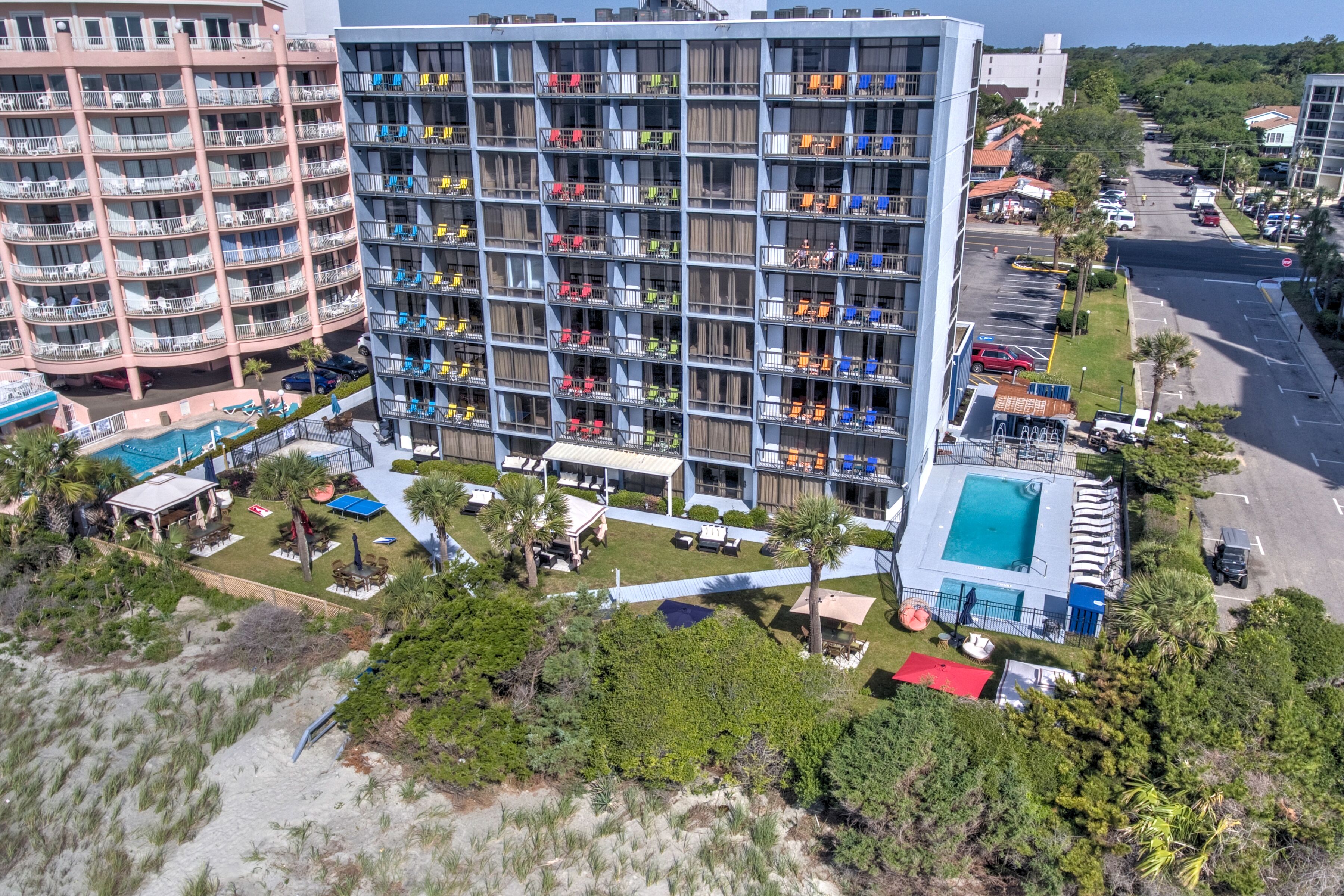 An aerial view of a multi-story building with balconies, a pool, and a parking lot surrounded by trees.