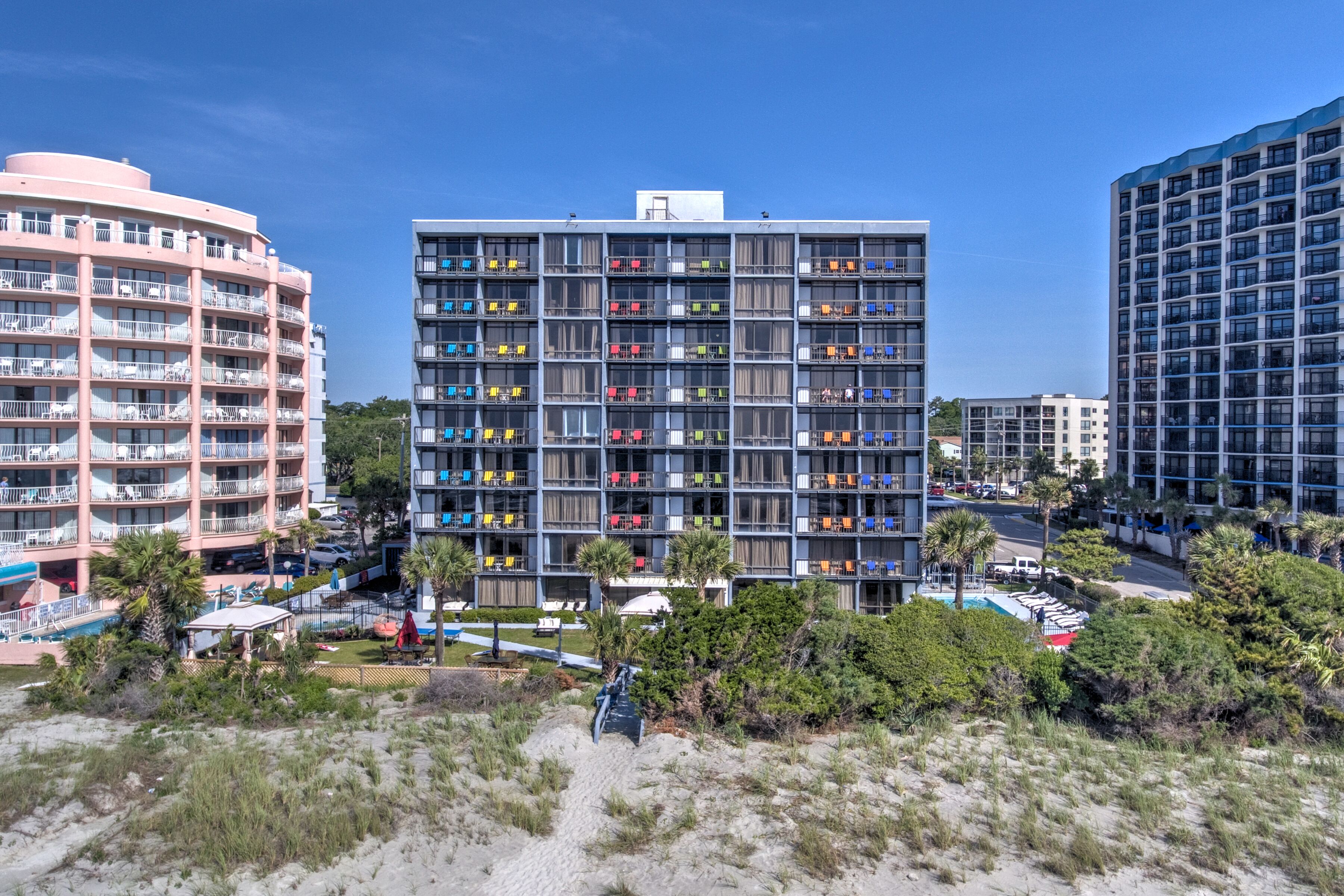 A large building with balconies and colorful chairs sits on a beach.
